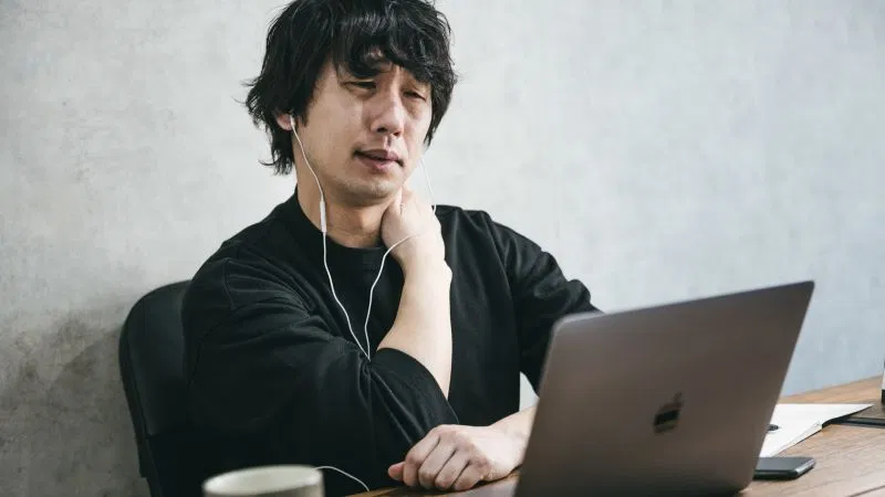 デスクワークで肩こりに悩む男性の写真